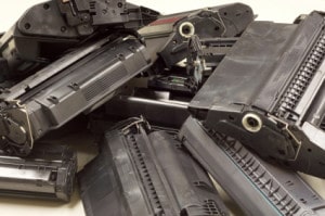 A pile of used black printer toner cartridges from laserprinters. Focus on most of the cartridges. All brands removed.